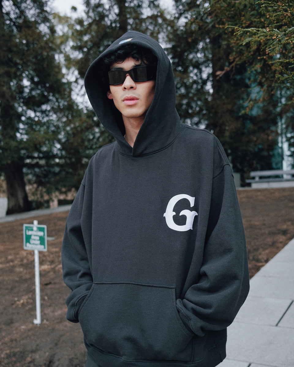 A model wearing a black Gardens & Seeds "G" Hoodie in Black